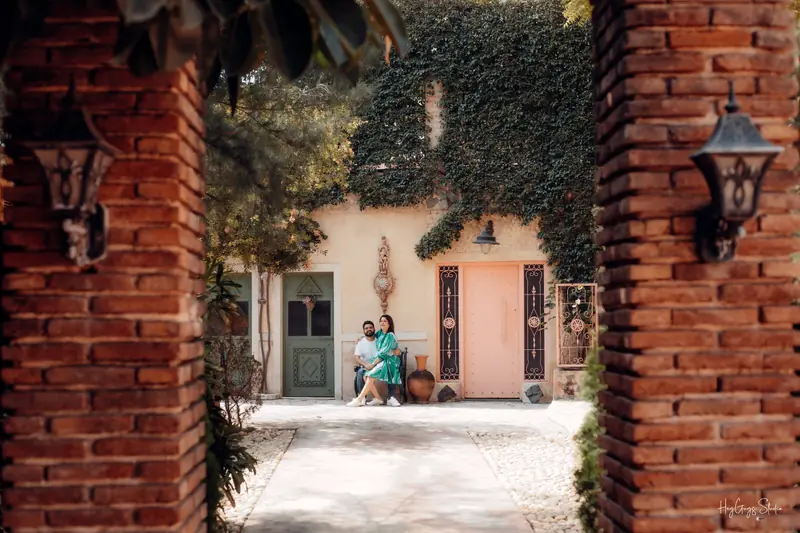 Wide view of a couple framed by a brick archway in a leafy villa courtyard