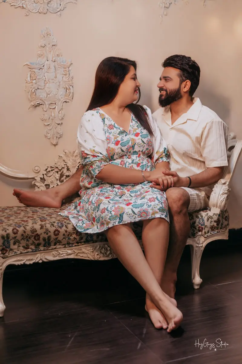 Couple seated on a vintage sofa beneath a chandelier during a pre-wedding shoot