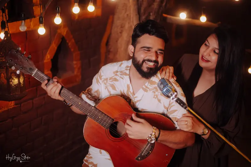 Groom-to-be serenading his partner on guitar beneath strings of warm fairy lights
