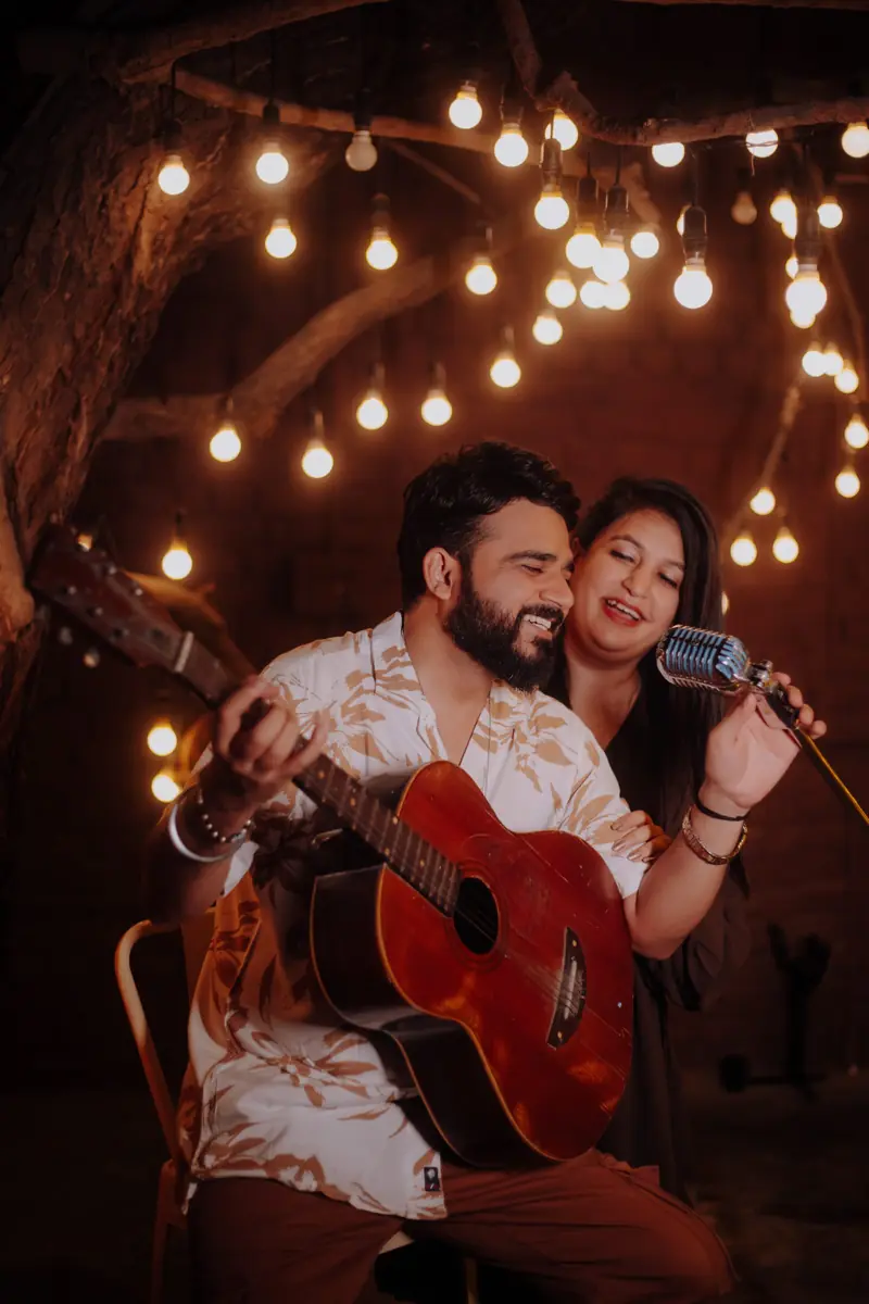 Couple singing together with a guitar and vintage microphone under fairy lights