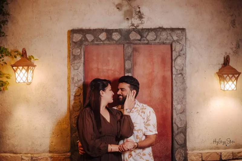 Couple framed by a weathered red door and hanging lanterns in the evening light
