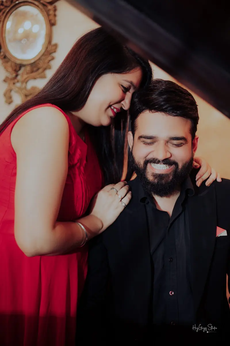 Couple laughing together beside an ornate mirror, the bride-to-be in a red gown