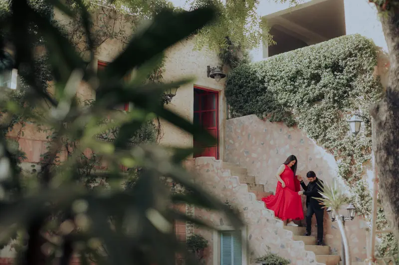 Couple on a villa staircase seen through soft green foreground leaves