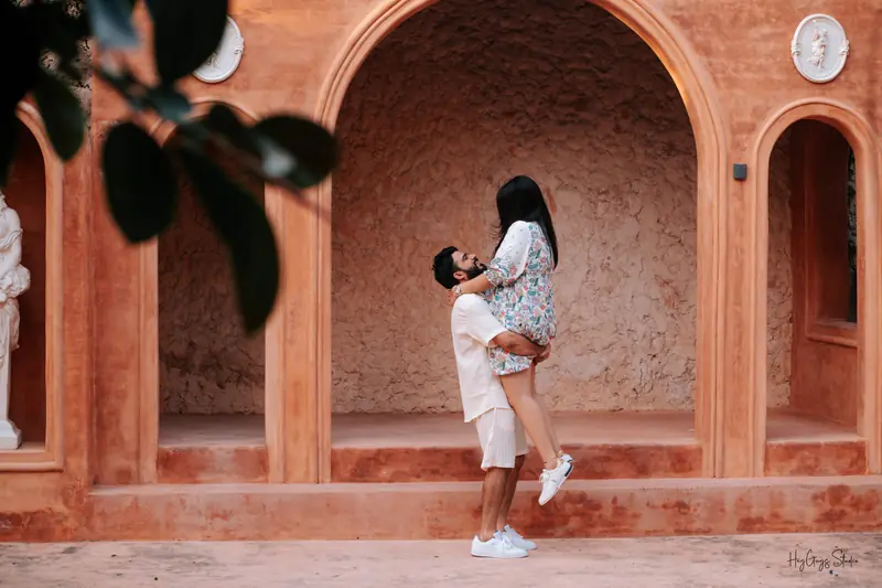 Groom-to-be lifting his partner in a terracotta arched corridor at golden hour