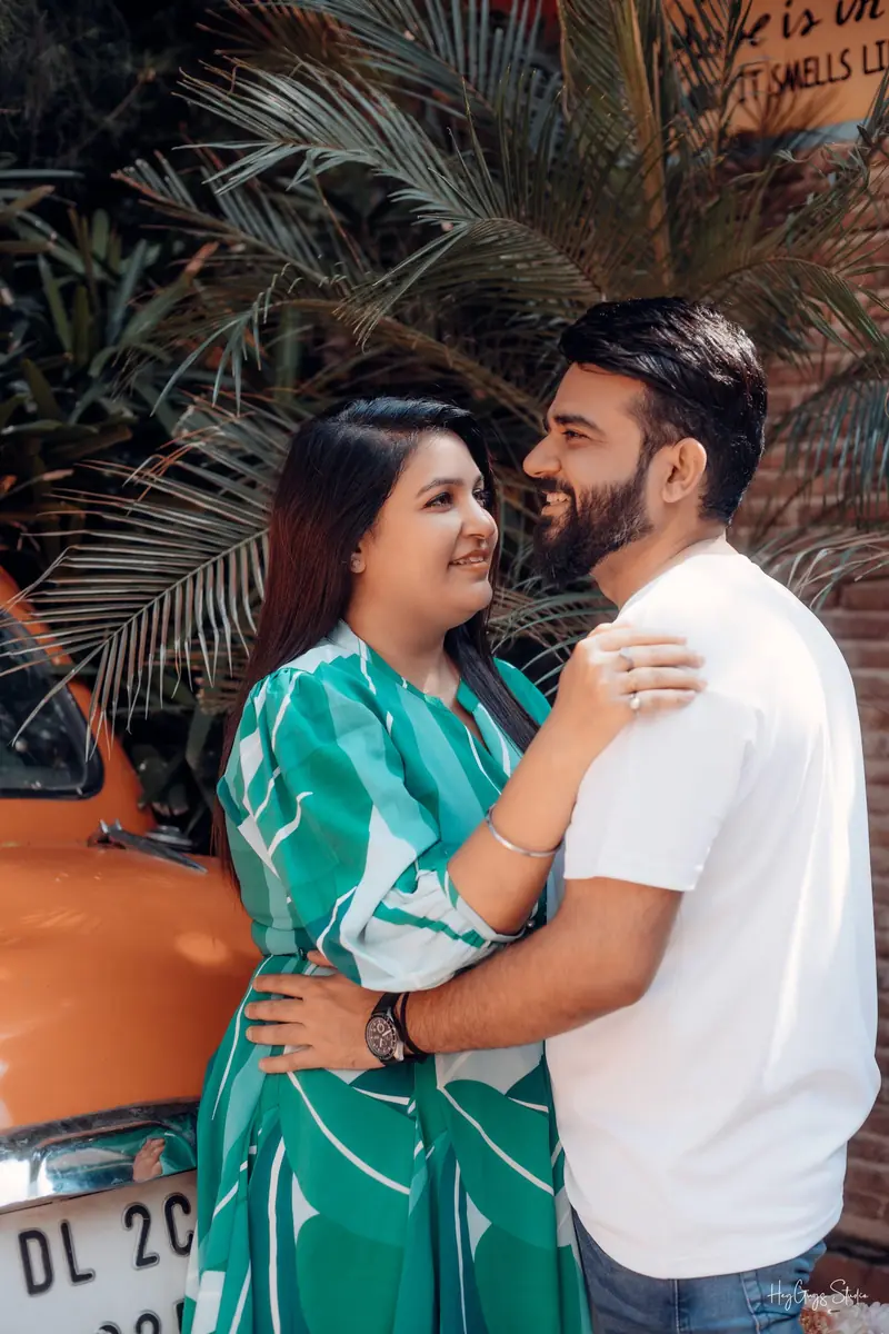 Couple embracing beside a vintage car and palm fronds at a pre-wedding location in Delhi NCR