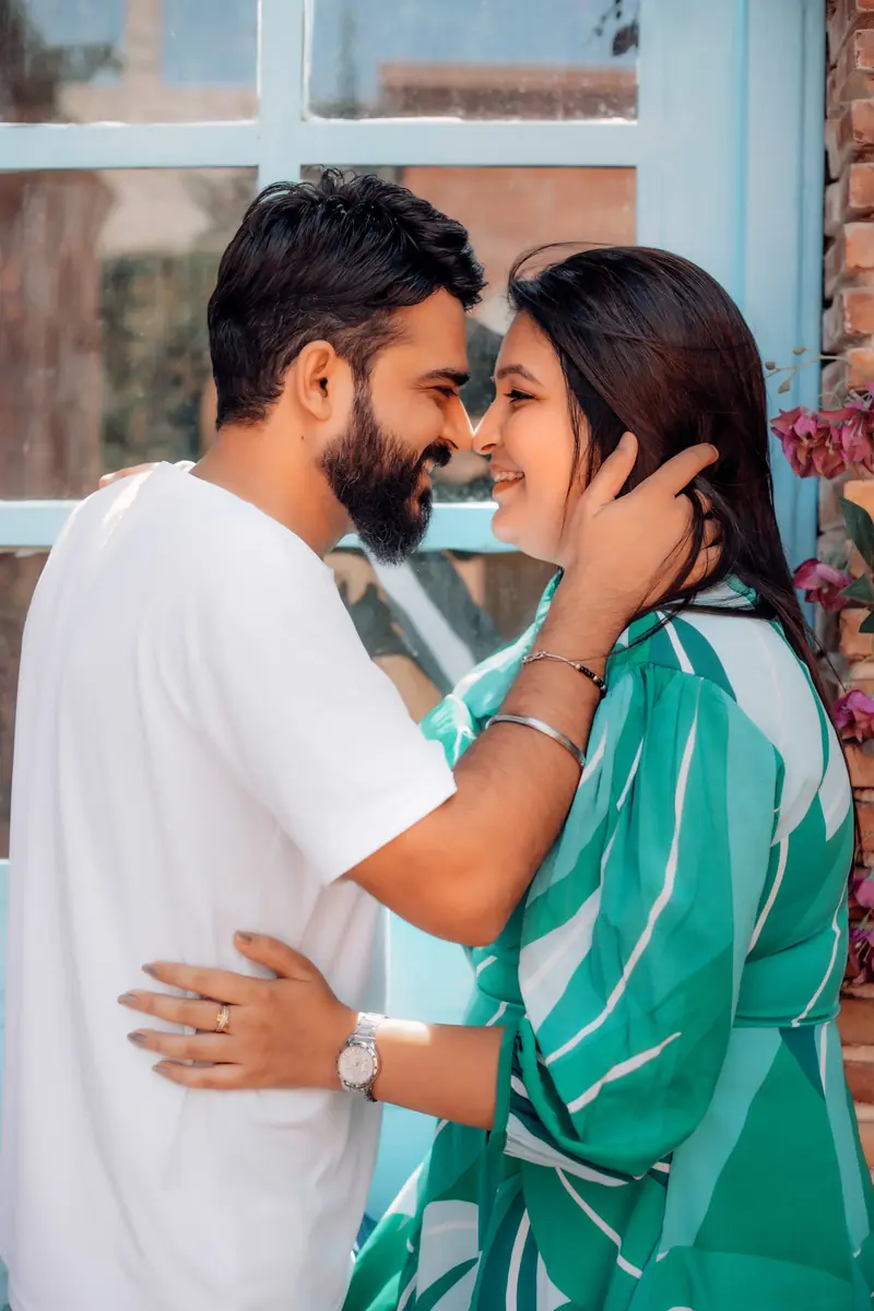 Groom-to-be cupping his partner's cheek beside a sunlit window during a pre-wedding shoot