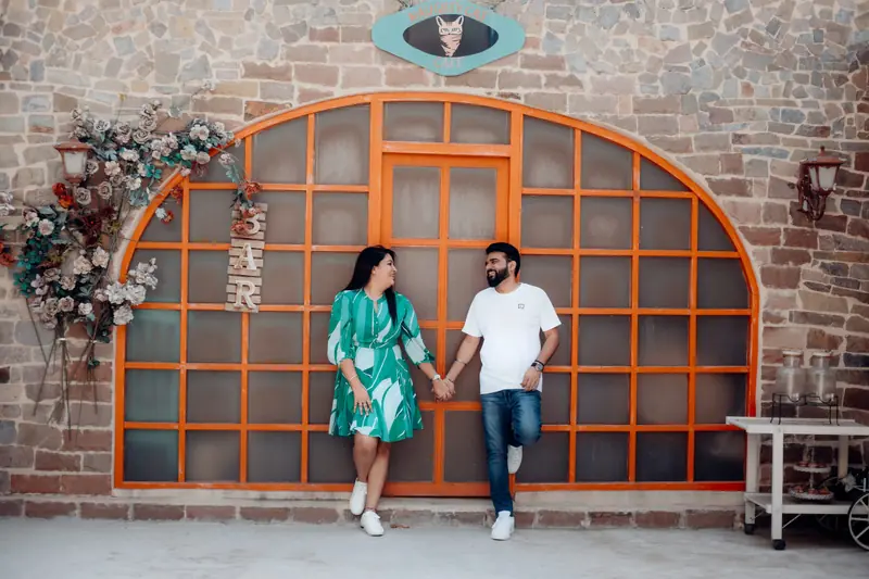 Couple holding hands in front of a bright orange arched doorway framed with flowers