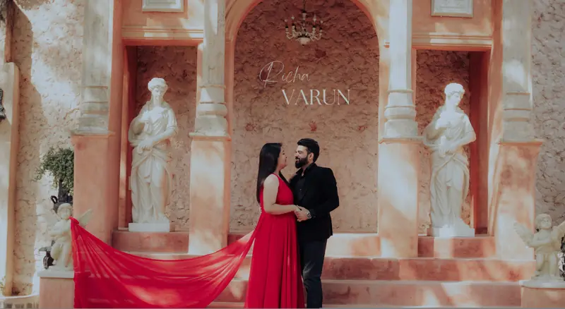 Couple posed in a classical statue colonnade with a sweeping red train