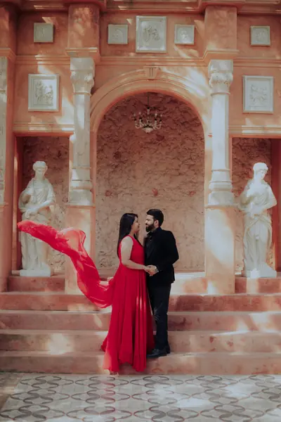Bride-to-be's red gown caught mid-air in a classical statue courtyard