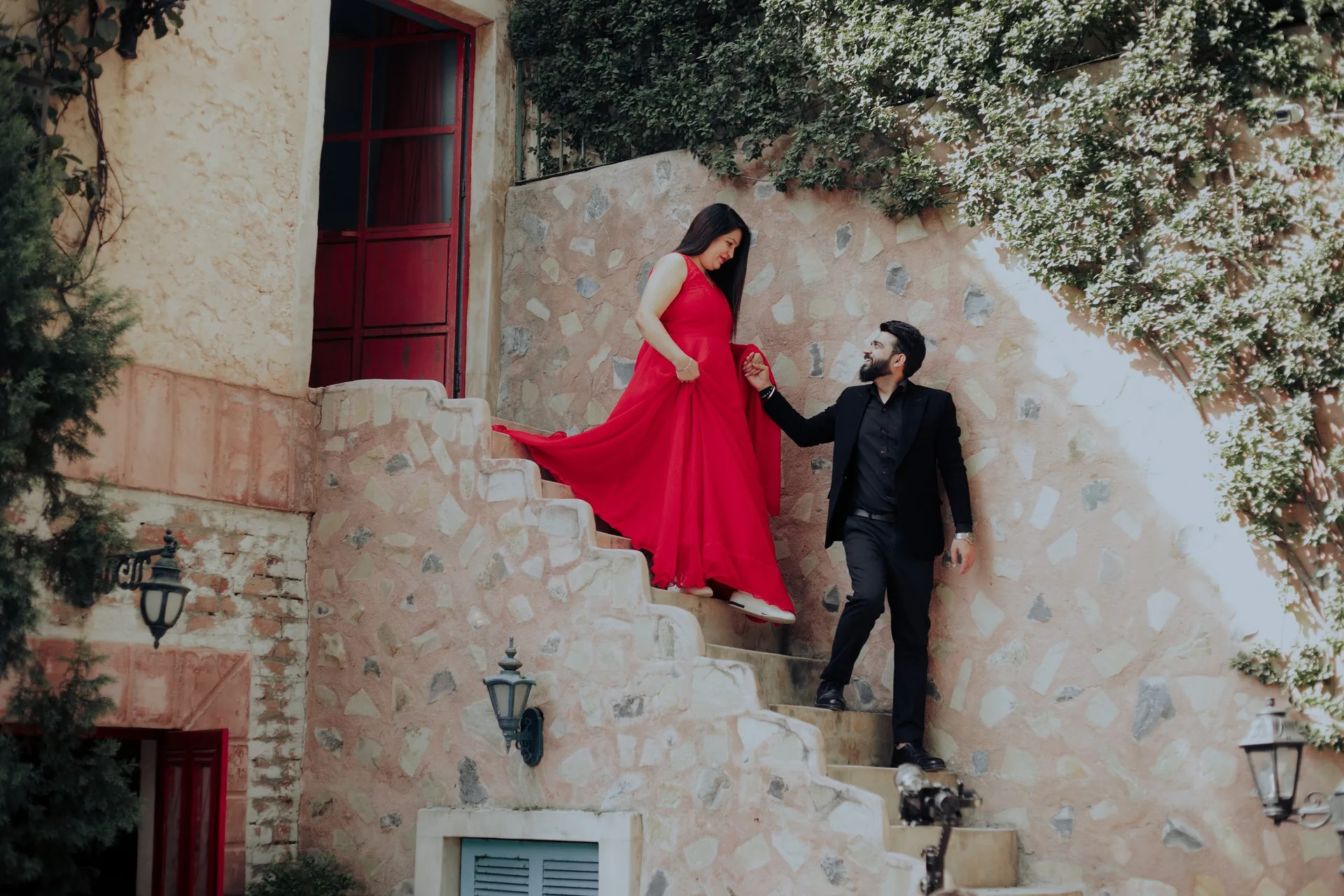 Bride-to-be in a red gown on a stone staircase, her train trailing behind her