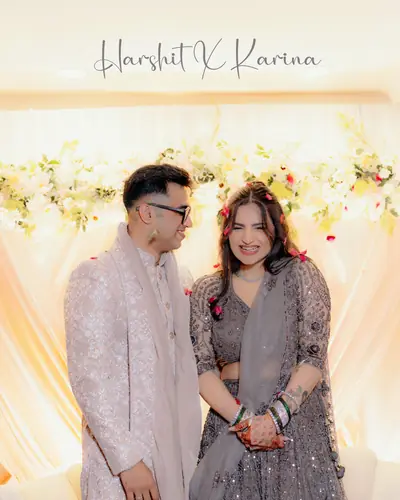 Newlywed couple in coordinated pastel wedding outfits before a floral and fairy-light mandap backdrop